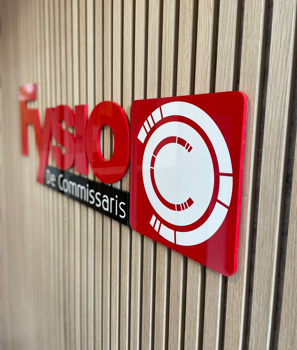 Het logo van Fysio de Commissaris op de lattenwand bij de ingang